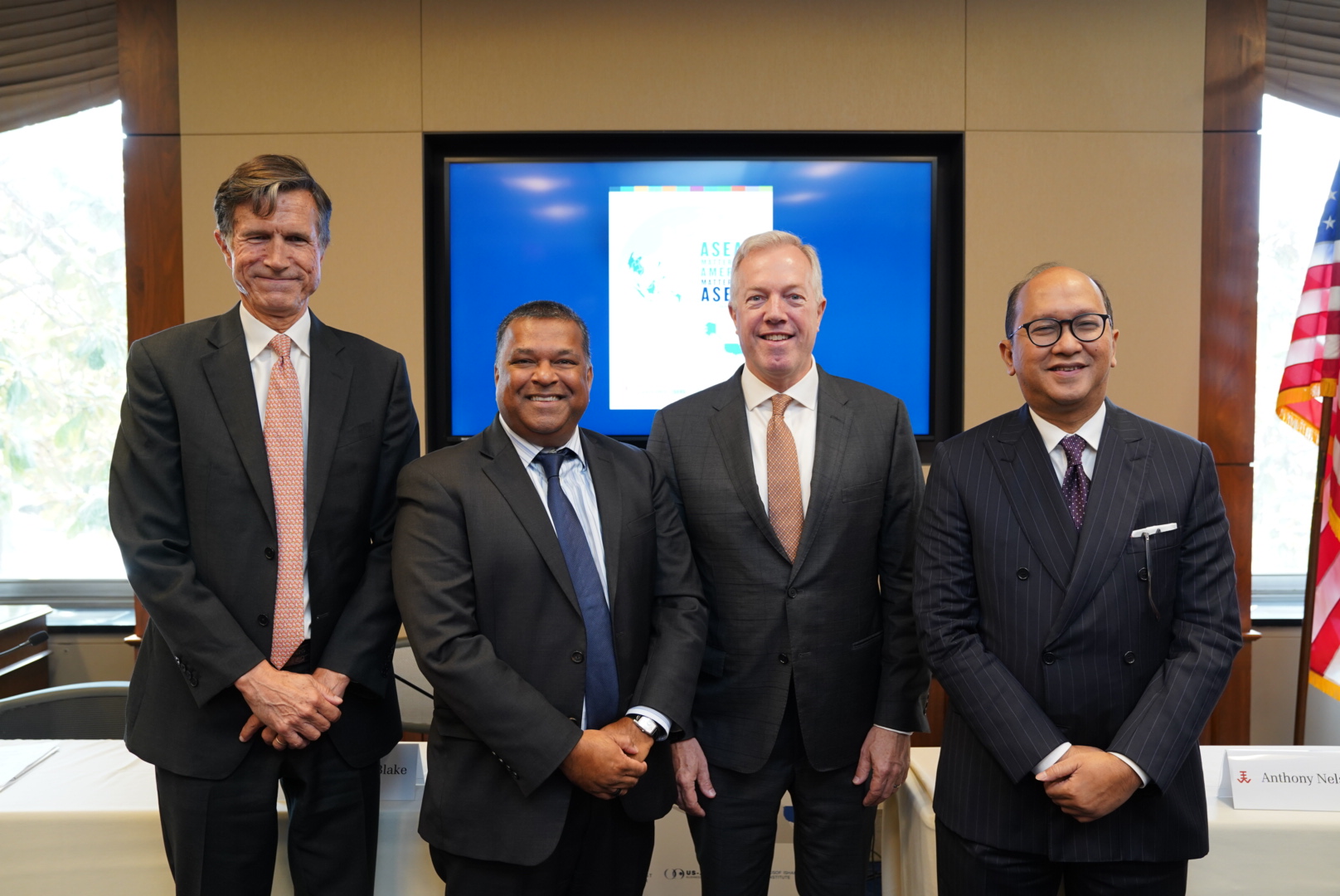 Four men in suits (Amb. Robert Blake (far left), H.E. Rosan Roeslani (far right), and Amb. Ted Osius (center right). Dr. Satu Limaye (center left) pose in front of a screen with the ASEAN Matters for America cover.