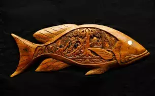 Carved wood in the shape of a fish, containing a detailed carving within of a scene from a Palauan legend