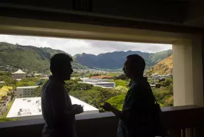 two students talk on the balcony of Hale Manoa overlooking Manoa valley
