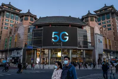 People cross a road in front of an Apple store advertising 5G capable phones at a shopping district in Beijing, China