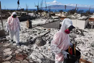 Volunteers in protective gear help residents search through the remains of burnt homes in Lahaina.