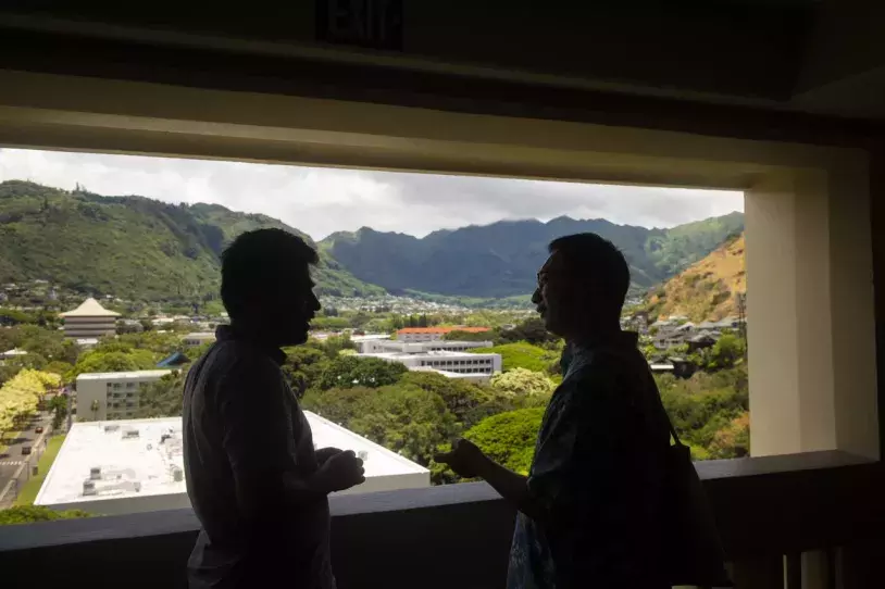 two students talk on the balcony of Hale Manoa overlooking Manoa valley