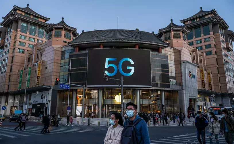 People cross a road in front of an Apple store advertising 5G capable phones at a shopping district in Beijing, China