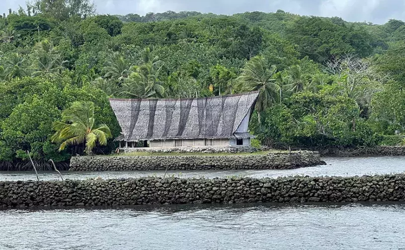 A thatched-roof men's house in Yap sitting on stonework above the waterline
