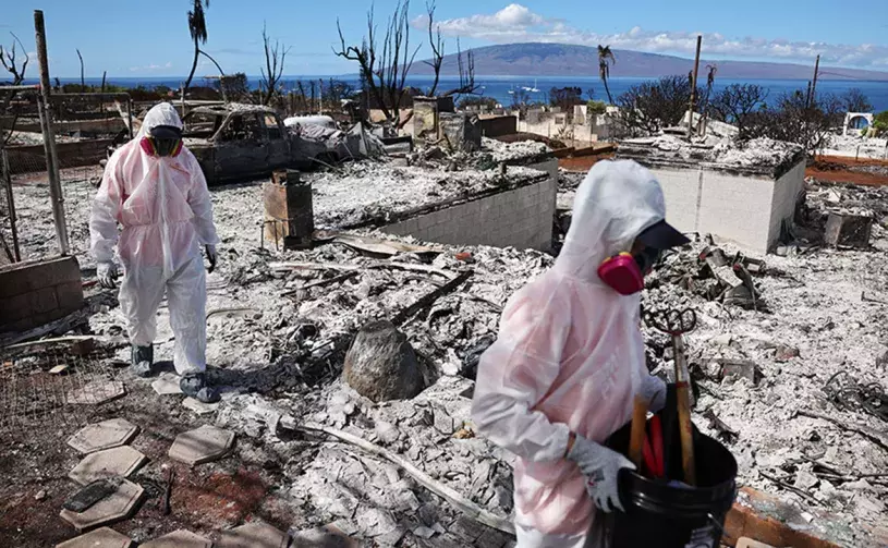 Volunteers in protective gear help residents search through the remains of burnt homes in Lahaina.
