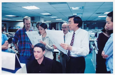 Early 2000s newsroom photograph of Melvin Goo reviewing a proof with editors.