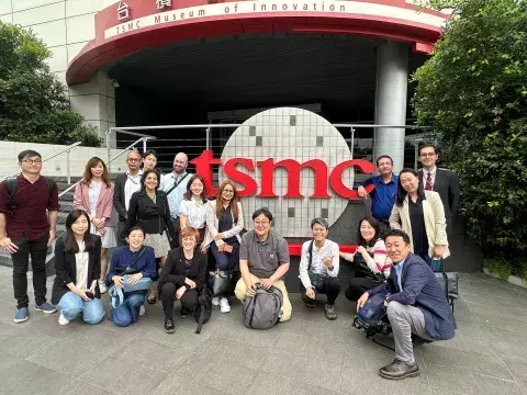 A group of people stand casually around a TSMC logo sign.